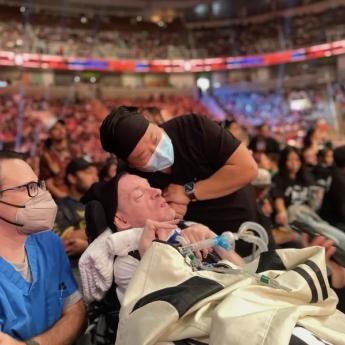 A man in a wheelchair attends a WWE match alongside two nurses, one in blue scrubs and one in black